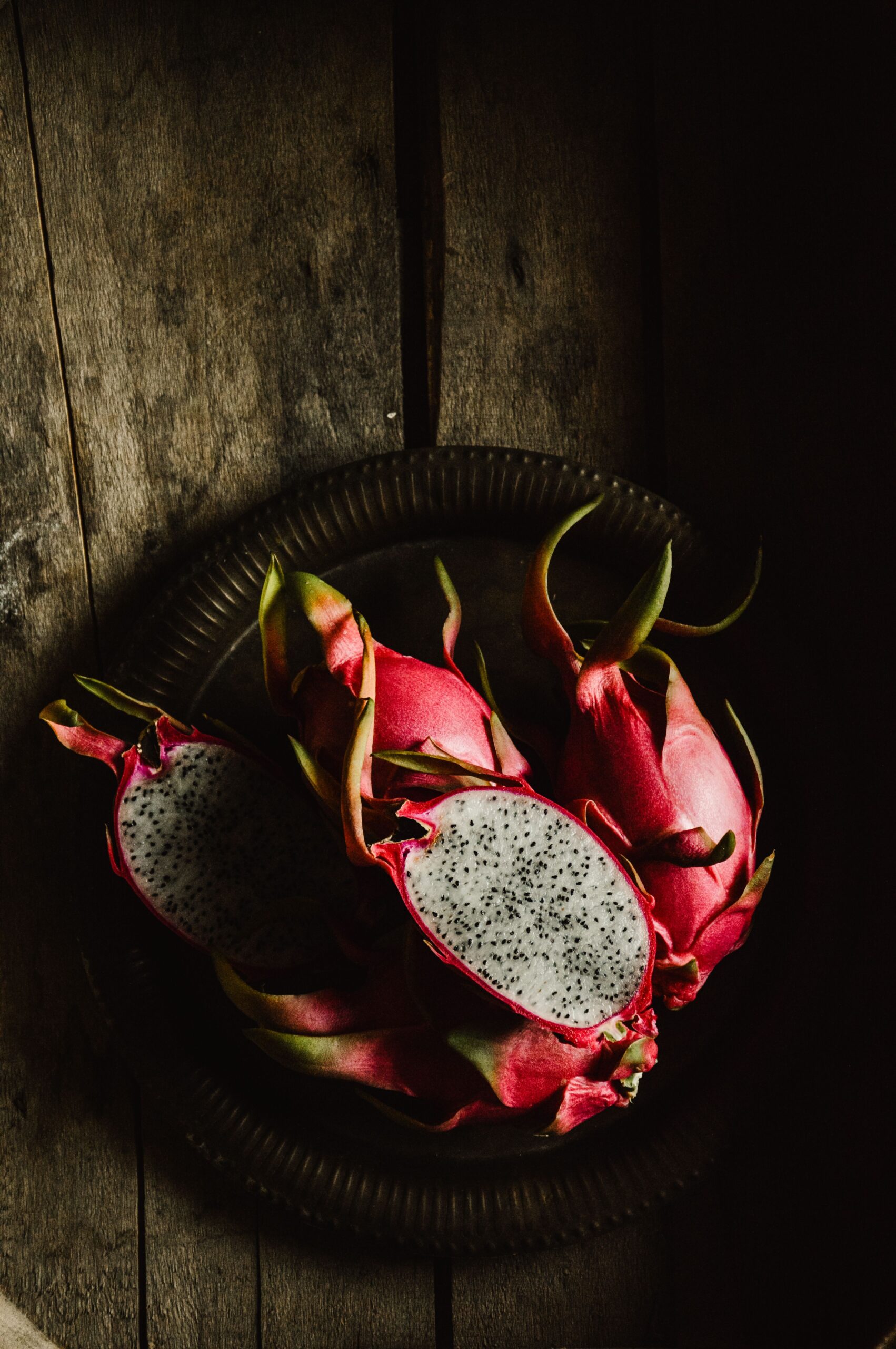 Moody still life featuring dragon fruits on a wooden table in dim lighting.